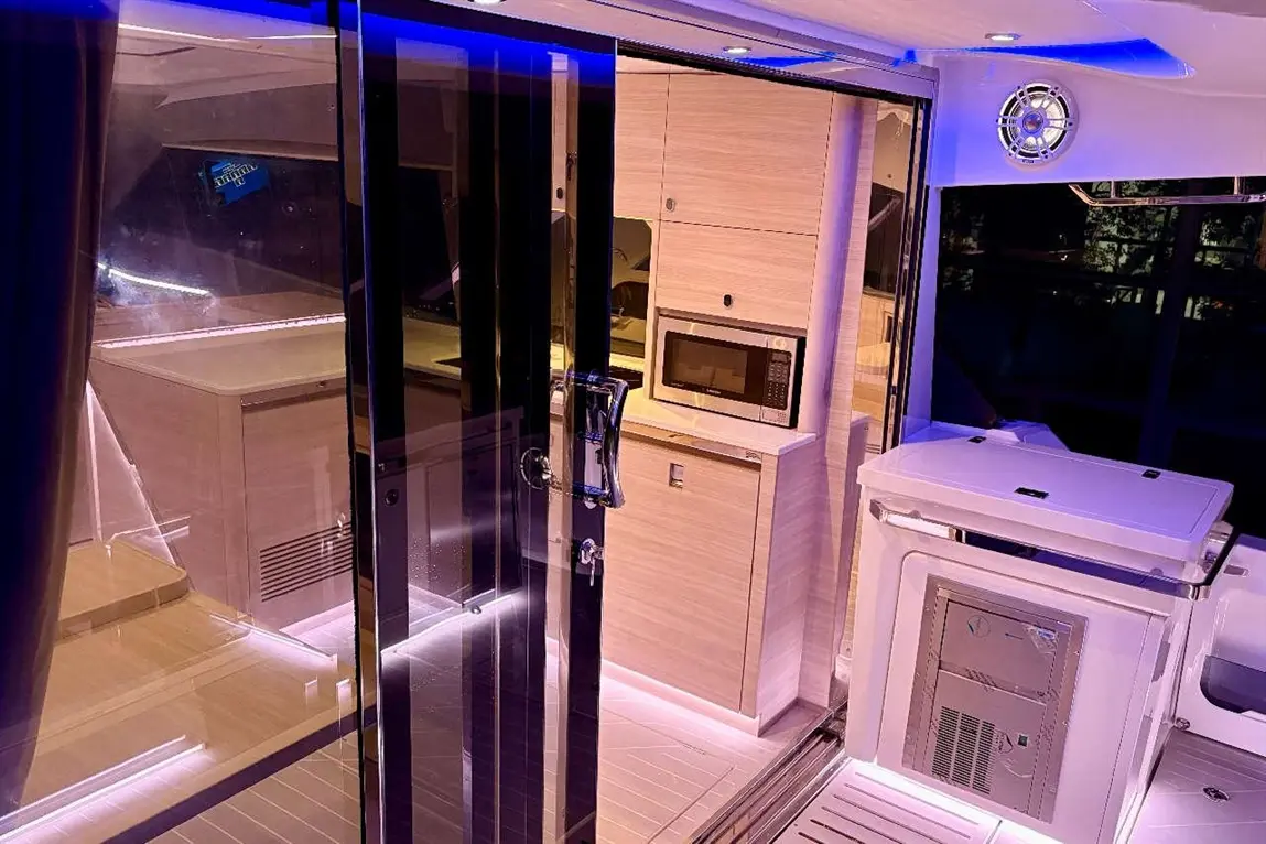 Modern boat interior featuring sleek cabinetry, a microwave, and illuminated underfoot lighting. Glass doors enhance spaciousness.